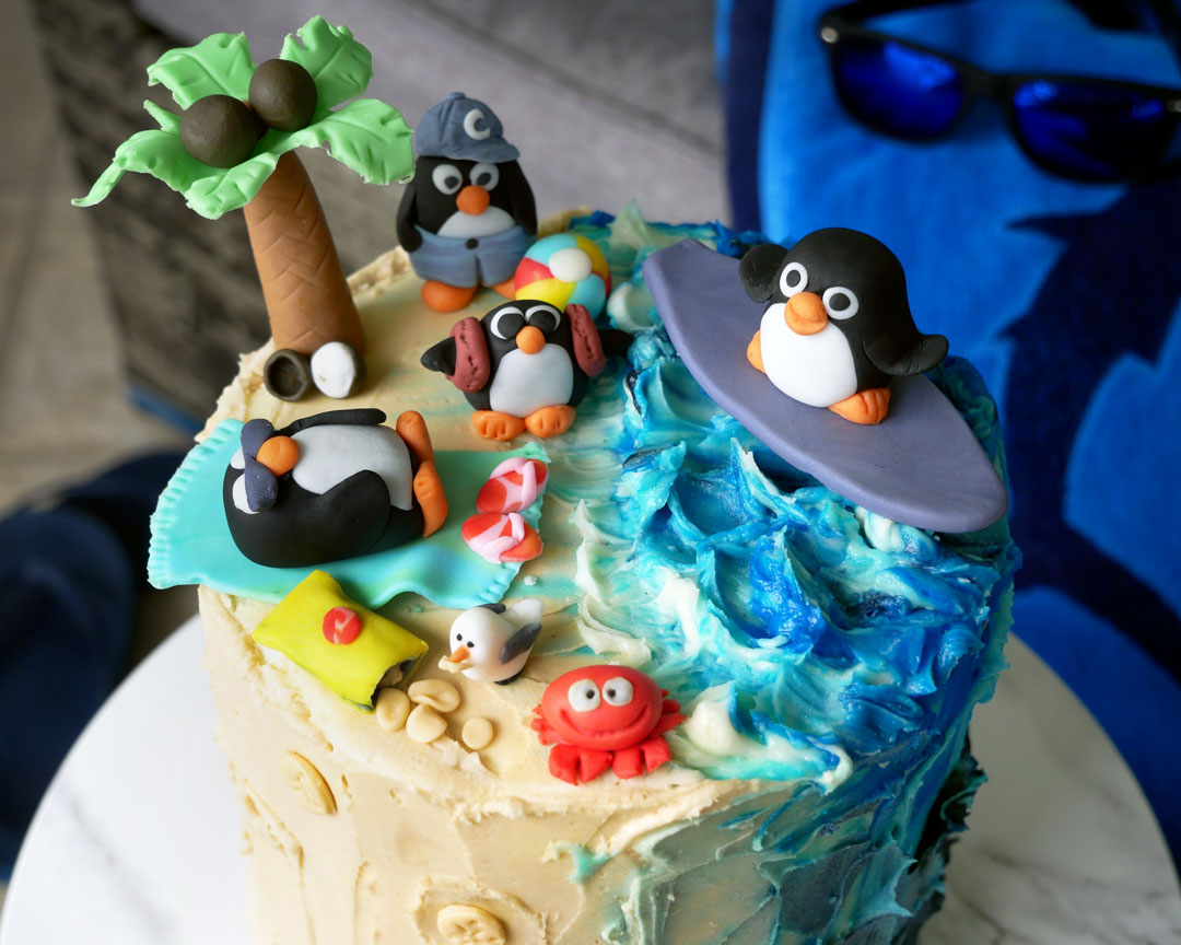 Penguins on Vacation - fondant penguins at a beach scene, on a triple chocolate oreo crunch cake decorated with white chocolate buttercream to look like sand and ocean waves.