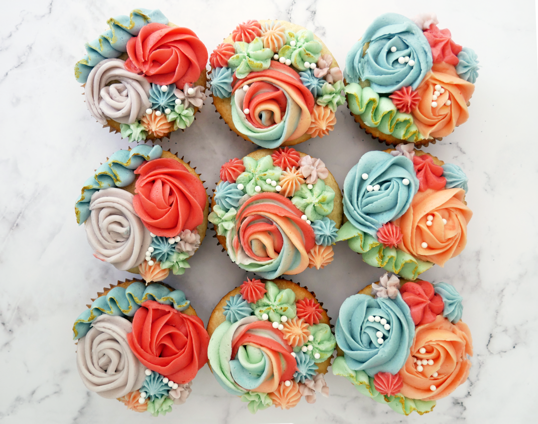 Colorful spring piped cupcake set, featuring peach jam filled Magnolia bakery-style cupcakes, topped with gold luster dust and Brandy buttercream flowers!