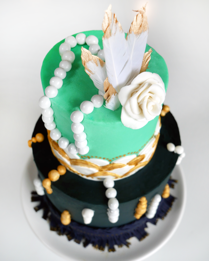 Roaring '20s cake, Great Gatsby themed cake, two tier blue and gold cake with scalloped edges, pearls, fringe, and gold with a fondant flower. 